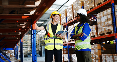 Dos mujeres revisando las entregas en la bodega. Al fondo hay más cajas.
